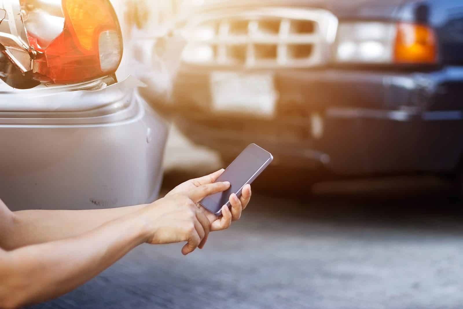 Driver photographing the scene on a smartphone at the roadside after a Dallas crash involving an uninsured driver