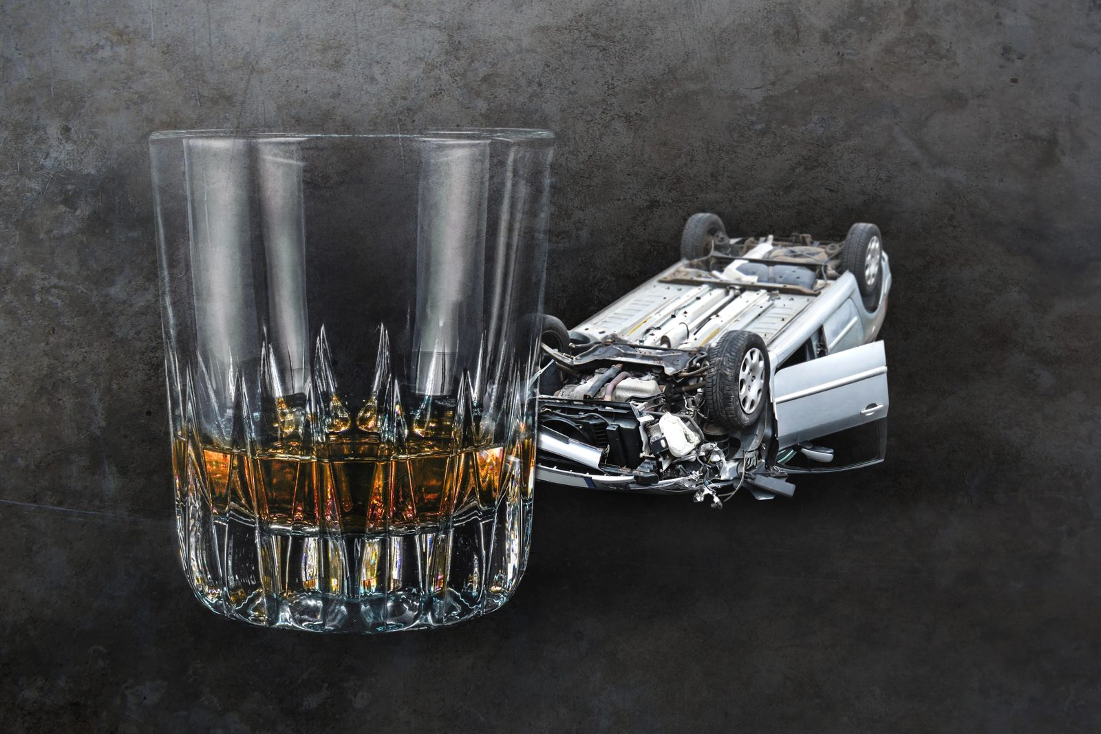 Whiskey glass beside an overturned wrecked car, representing a drunk driving accident.