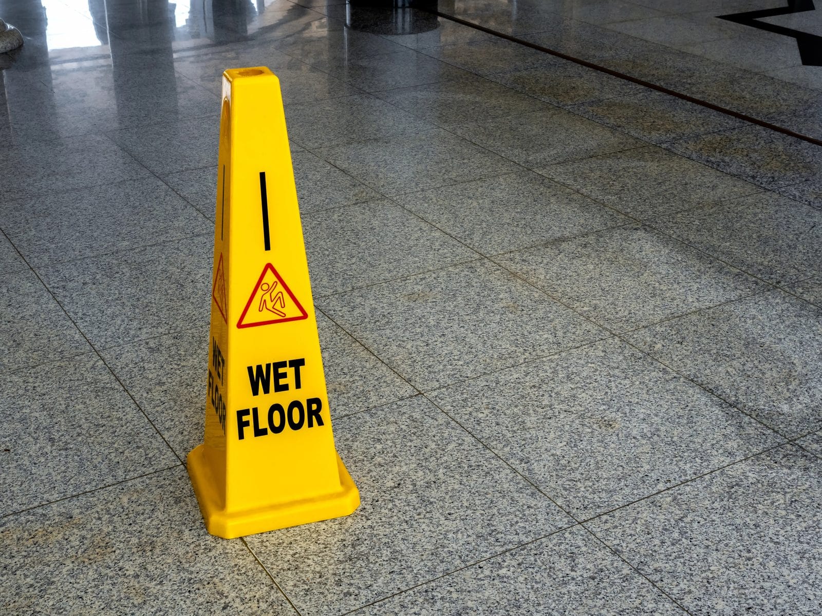 Yellow wet floor caution sign on a tiled floor warning of a slip and fall hazard