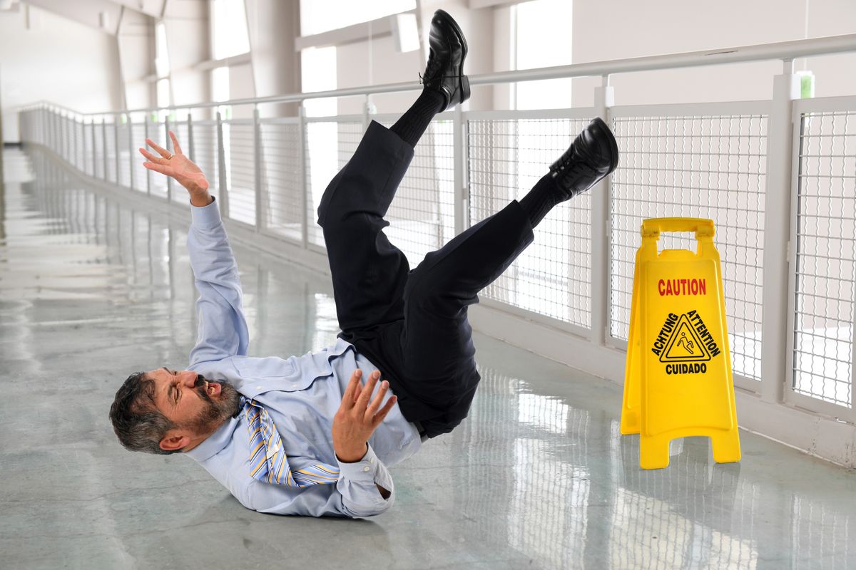 Man slipping and falling next to a yellow caution wet floor sign in Olive Branch, Mississippi