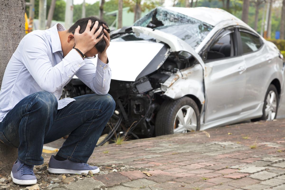 Distraught driver beside a wrecked car after a collision with an uninsured motorist in Olive Branch, Mississippi