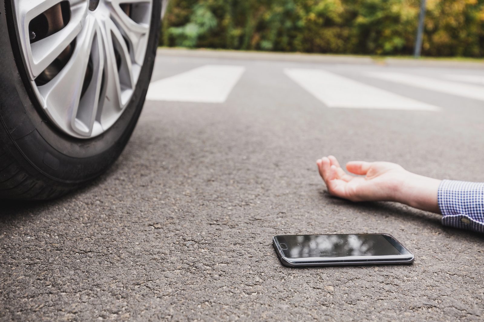 A pedestrian lies in the road in front of a car’s headlights at night after being hit while crossing the street.