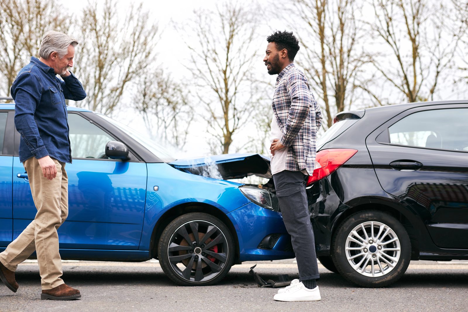 Two drivers inspecting the damage to their cars after a rear-end collision on the road.