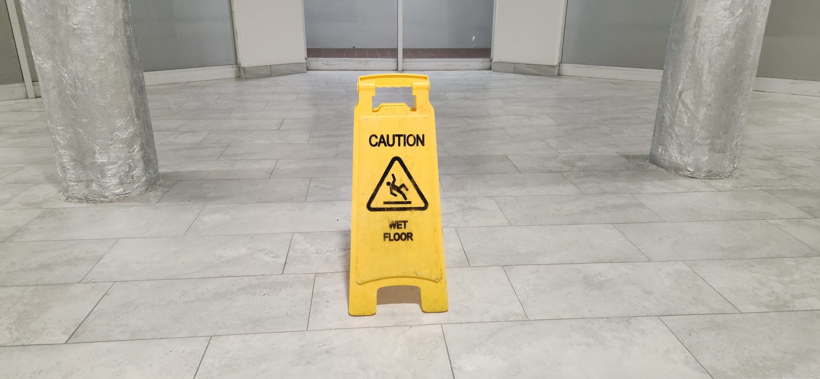 Yellow caution wet floor sign on a tiled floor in a building hallway, a common slip and fall hazard
