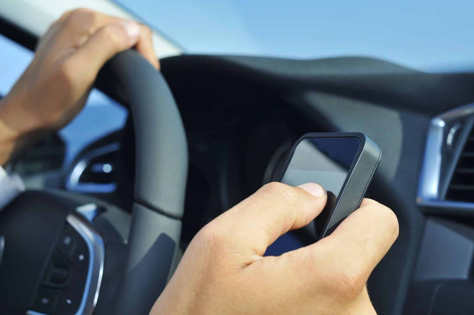 Rideshare driver holding a smartphone with one hand on the wheel, illustrating an Uber or Lyft driver using the app.